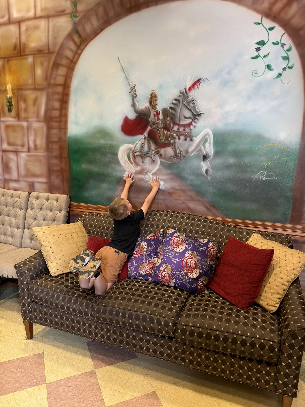 A child kneeling on the couch reaching up toward the painted knight on horseback in the castle waiting room at Preferred Pediatrics